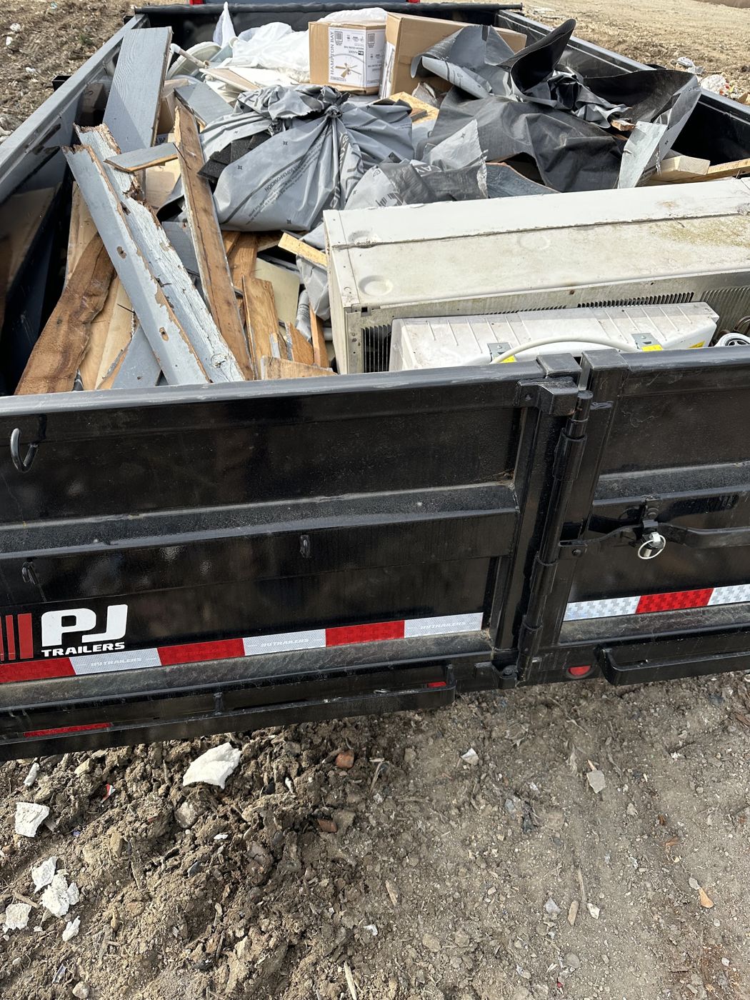 Dump trailer loaded with lumber, roofing felt and an old appliance